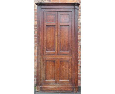 A large George III free standing oak corner cabinet, with moulded cornice above four panelled cupboard doors enclosing shelve