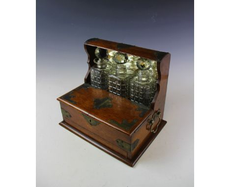 A late Victorian gaming tantalus, with three moulded glass decanters and stoppers and hinged top enclosing a compartmented al