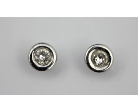 A pair of diamond set stud earrings, each designed as a solitaire diamond within a rub-over collet white metal setting, with 