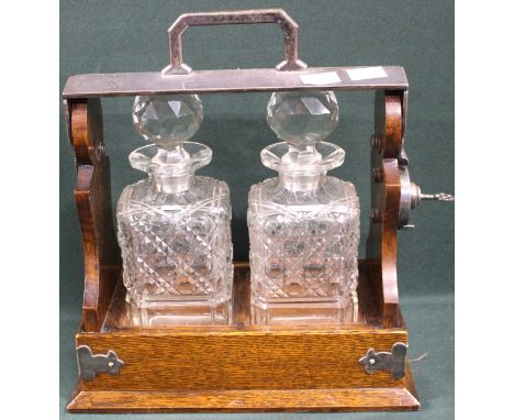 An early twentieth century oak two decanter tantalus with plated mount and handle, 27cm wide x 30cm high