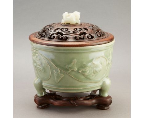 Circular form with lonquan celadon glaze and relief decoration, resting on three short curved legs. Carved wooden cover with 
