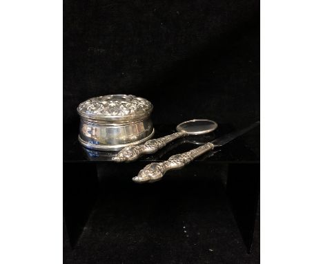 A circular silver trinket box in Victorian style, the hinged cover repousse decorated with a bird, foliate scrolls and a vaca