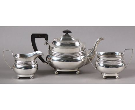 A George V silver three-piece tea service in the regency style, of compressed oblong form, each on four ball feet; Birmingham
