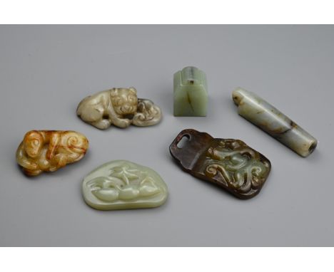 SIX CHINESE JADE CARVINGS. Comprising: a celadon jade pendant depicting a trees in landscape, a dark brown pendant carved wit