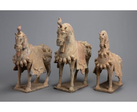 THREE NORTHERN WEI DYNASTY-STYLE POTTERY MODELS OF HORSES. Each modelled standing foursquare, wearing a saddle cloth, belled/