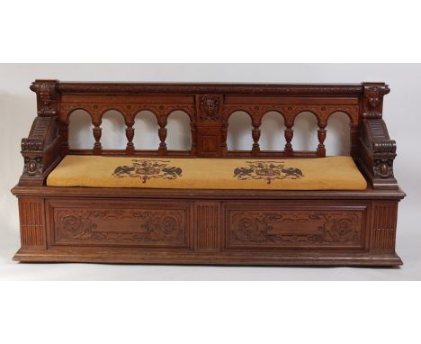 A late 19th century Continental oak settle, having an arcaded back with applied mask carvings, architectural scroll arms to a