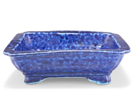 A CHINESE BLUE-GLAZED DISH, rectangular with inverted corners, the thickly potted body with mottled blue glaze, raised on fou