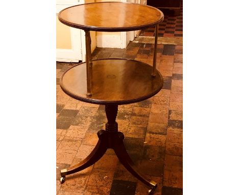 A George III mahogany two tier dumbwaiter, circa 1820, supported on three brass pillars above a twisted carved collumn on sab