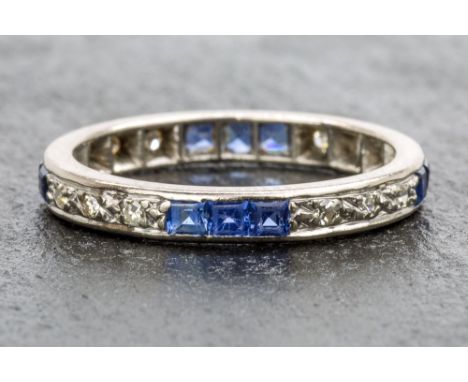 An 18ct white gold, sapphire and diamond eternity ring 1920s-30s, set with alternating sets of three square cut cornflower bl