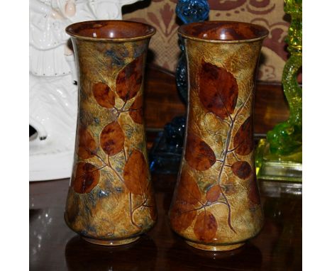 A matched pair of Royal Doulton stoneware vases of waisted cylindrical form, decorated with ash leaves on a blue and light br