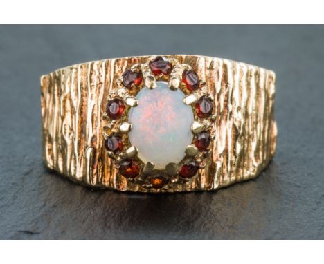 A 9ct gold, opal and garnet cluster ring the broad bark effect ring set with an oval opal within a border of small round cut 