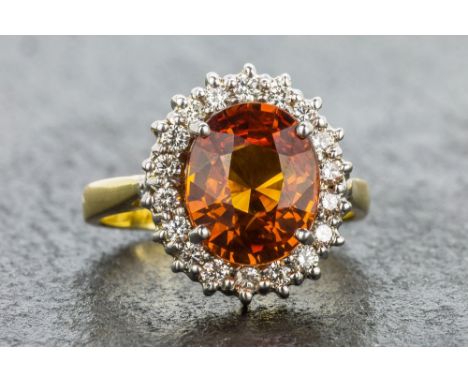 An 18ct white and yellow gold, orange sapphire and diamond cluster ring the oval cut 4 carat sapphire within a border of eigh