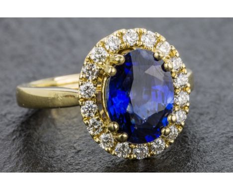 An 18ct yellow gold, sapphire and diamond cluster ring the 3.04 carat sapphire of fine colour, within a border of eighteen ro