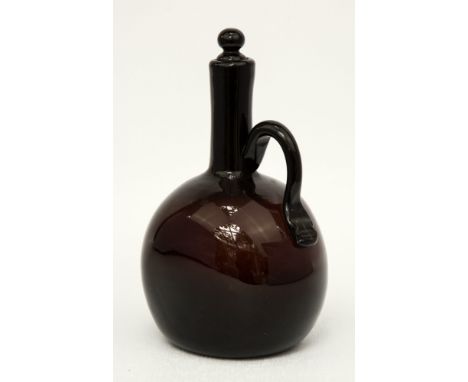 A 19th century dark amber glass wine flagon of flattened ovoid form with scroll handle and finial stopper, 7.75in. (19.75cm.)