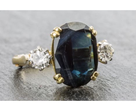 An 18ct gold and platinum blue-green sapphire and diamond three stone ring the oval cut sapphire of unusual dark blue-green c