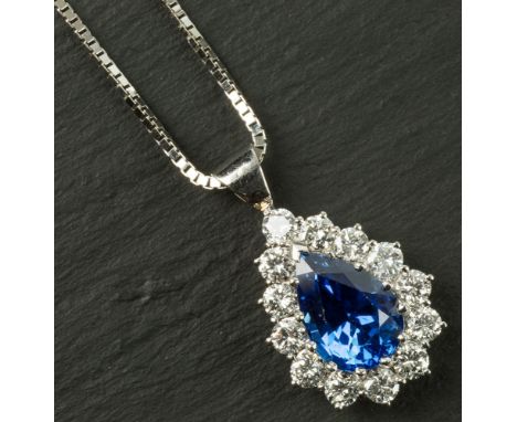 An 18ct white gold, sapphire and diamond cluster pendant the pear cut sapphire within a border of thirteen round brilliant cu