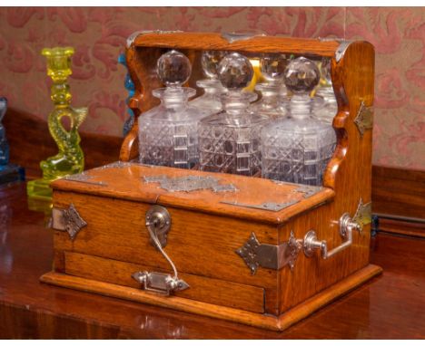 A Victorian oak three bottle tantalus with pierced silver plated mounts and handles, mirrored back, with three matching cut g