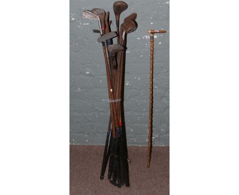 A collection of vintage golf clubs along with an antler handled walking stick.