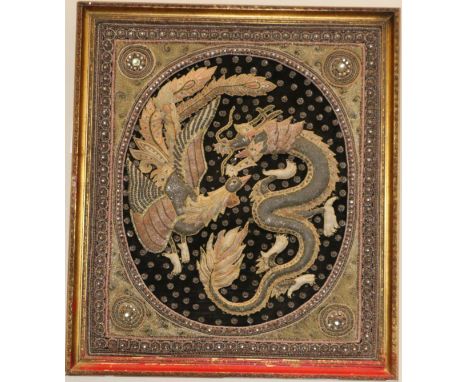 A South East Asian embroidery panel worked in various stitches and depicting a dragon and phoenix, now framed, 78cm by 66cm  