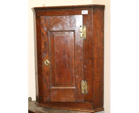 < An 18th century oak hanging corner cupboard, fielded panel door with brass H shaped hinges enclosing a green painted interi