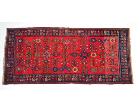 East Turkestan rug, Khotan, the abrashed crimson field of angular vines enclosed by indigo trefoil borders, 258cm by 123cm  V