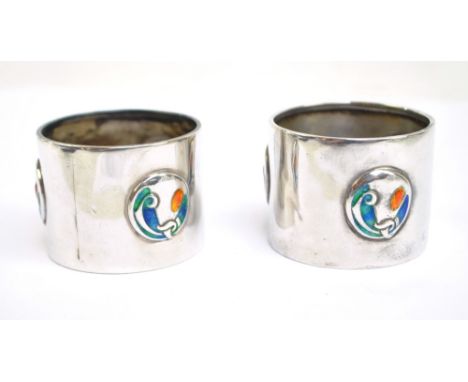 WILLIAM HAIR HASELER; a pair of Edwardian hallmarked silver Arts and Crafts enamel decorated napkin rings, each set with thre