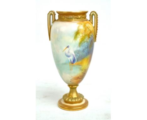 A Royal Worcester hand painted gilt heightened twin handled vase decorated with a stork standing in a riverbed, puce marks to