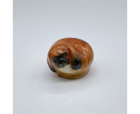 Hand painted porcelain figure of a curled up Chinese toy dog; light brown glaze with black highlights. Doulton backstamp. Iss