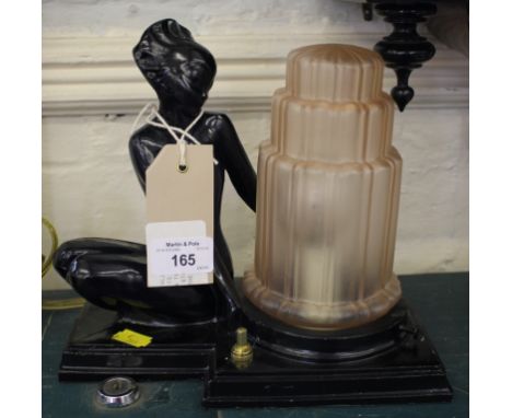 A blacked metal Art Deco table lamp, in the form of a kneeling nude holding the pink glass shade, 21cm high