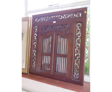 A carved hardwood Indian style wall mirror with pierced foliate carving and two grille doors enclosing the mirror, 90 x 80 cm