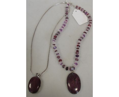 A collet mounted ruby cabochon pendant on a silver chain, together with another similar on a hardstone bead necklace (2) 