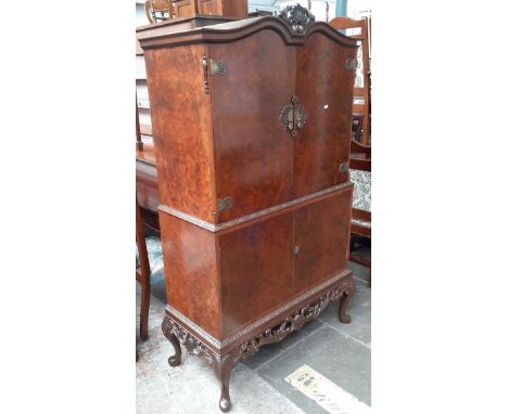 A mid 20th century burr walnut drinks/cocktail cabinet with carved frieze, mirrored interior and slide out serving tray, the 