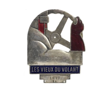 A 1917 'Les Vieux du Volant' enamelled car badge,in the form of a driver at the wheel, nickel-plated badge enamelled in red a
