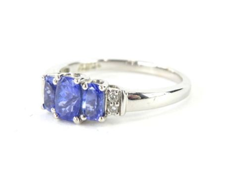 An 18ct white gold dress ring, claw set with three graduated bluey/purple stones, possibly tanzanite, flanked by small diamon