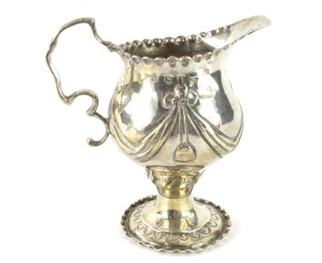 A George III silver cream jug, the helmet shaped body raised with garlands and flowers and initialled KTE, with shaped ear ha