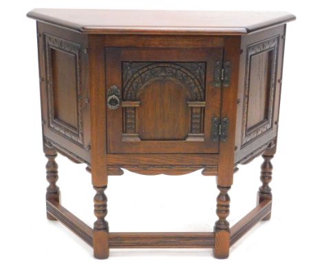 A Priory style oak side cabinet, the shaped top raised above a heavily carved door, with ring handle on turned legs joined by