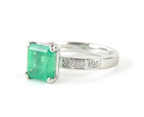 A platinum Art Deco design emerald and diamond ring, with claw set pale emerald stone, square cut, in four claw setting, with