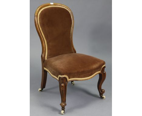 A Victorian mahogany spoon back nursing chair upholstered brown velour, &amp; on short cabriole legs with ceramic castors.