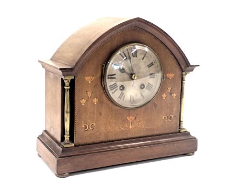 An Edwardian oak mantel clock, with arched top and boxwood tulip inlay and silvered dial, on columned supports with bun feet,