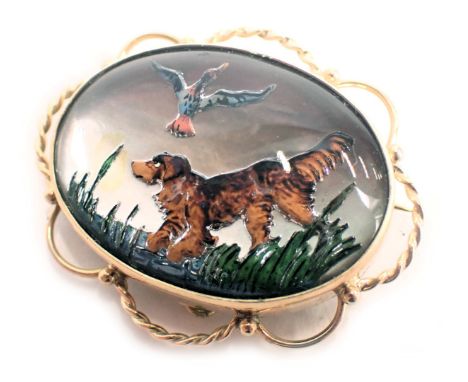 An oval animal brooch, with mother of pearl back, raised painted decoration of terrier and ducks in reeds, with looped outer 