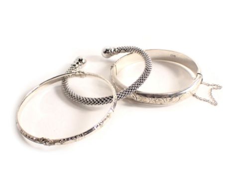 Three bangles, comprising a silver half hoop floral hinged bangle, a silver hammered design bangle, and a white metal torc ba