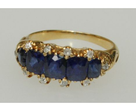 A Burmese sapphire five stone ring, channel set with graduated cushion cut sapphires flanked by diamond chips, claw mounted t