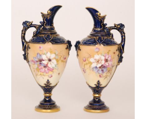 A pair of Royal Worcester pedestal ewers, each decorated with hand painted flowers against a blue ground, the foot and neck i