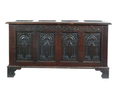 An 18th Century and later carved quadruple panelled oak coffer, the scroll frieze over an arched panelled front on bracket fe