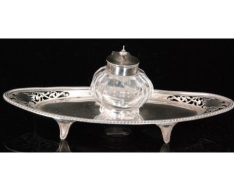 An Edwardian hallmarked silver inkstand, the oval base with foliate pierced border decoration and gadrooned rim centred by a 