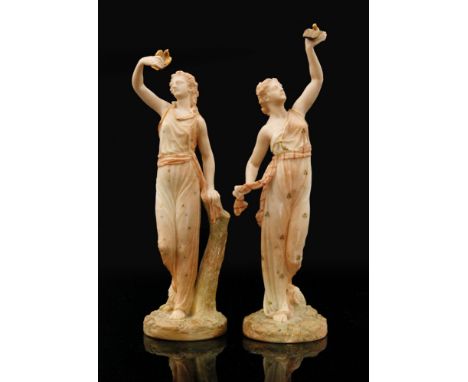 A pair of Royal Worcester blush ivory figures of Liberty and Captivity each holding a small bird, one set free, the other tra