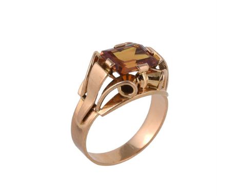 A 1940s French orange sapphire dress ring, the step cut orange sapphire with canted corners to scrolled gold coloured Odeanes