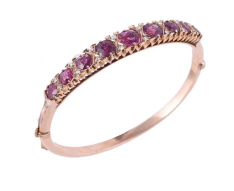 An early 20th century garnet and diamond hinged bangle, the graduated cushion shaped garnets interspaced with pairs of old cu