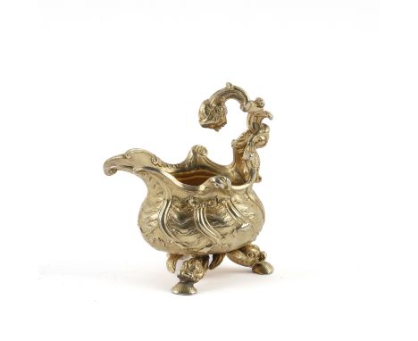 A SILVER GILT MID 18TH CENTURY STYLE CREAM JUGOf rococo design, raised on three dolphin form and scallop feet, the handle wit