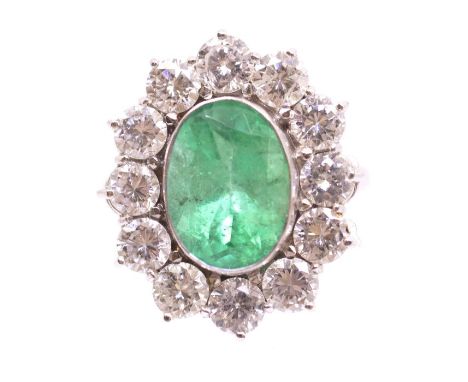 An emerald and diamond platinum cluster ring, comprising an oval emerald approx 3.10carats, rub- over set within a border of 